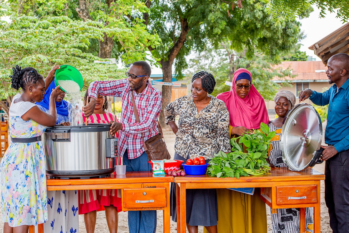 Educators and students look on as a meal is prepared in an electric cooker.