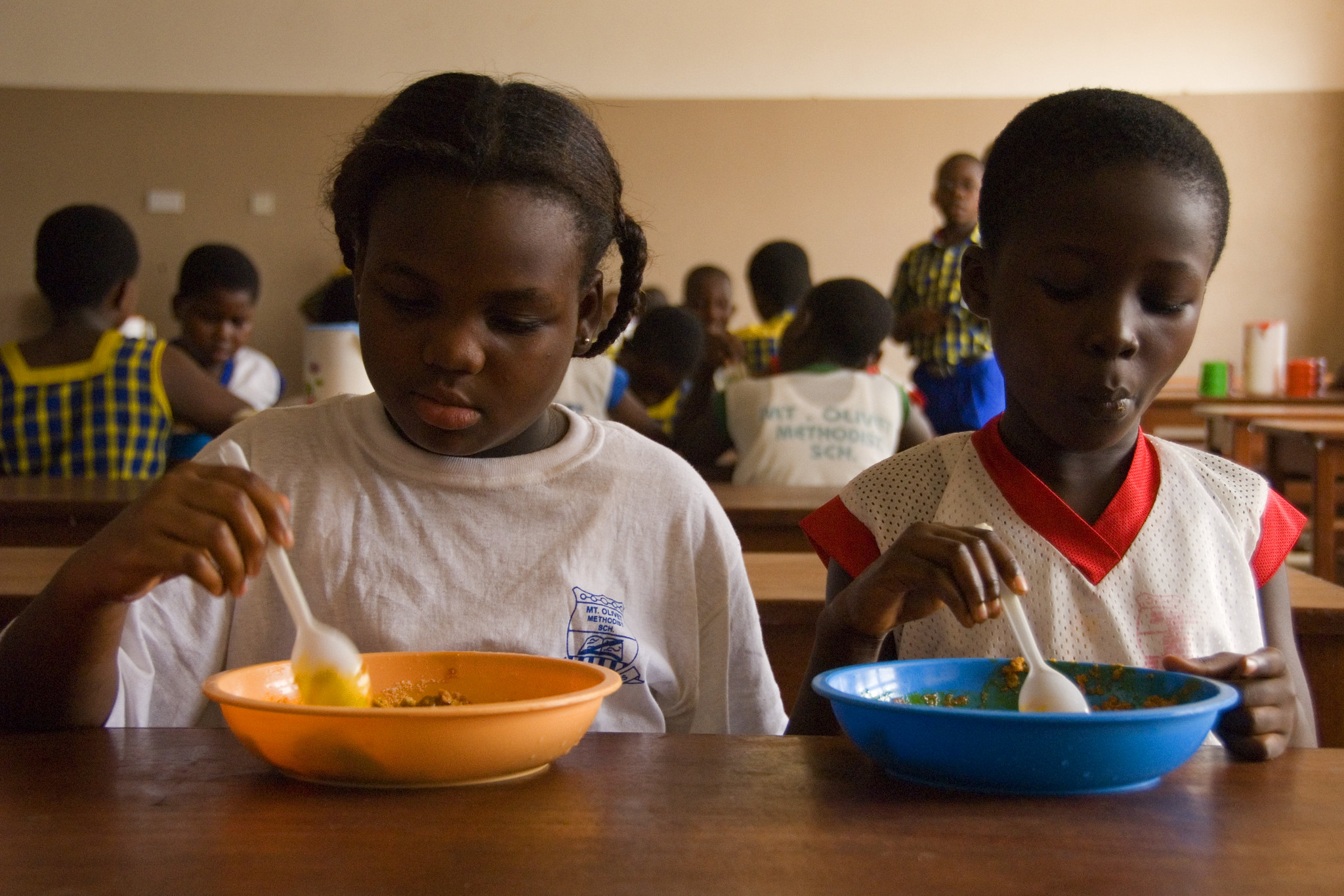 Two students in a classroom, eating food.